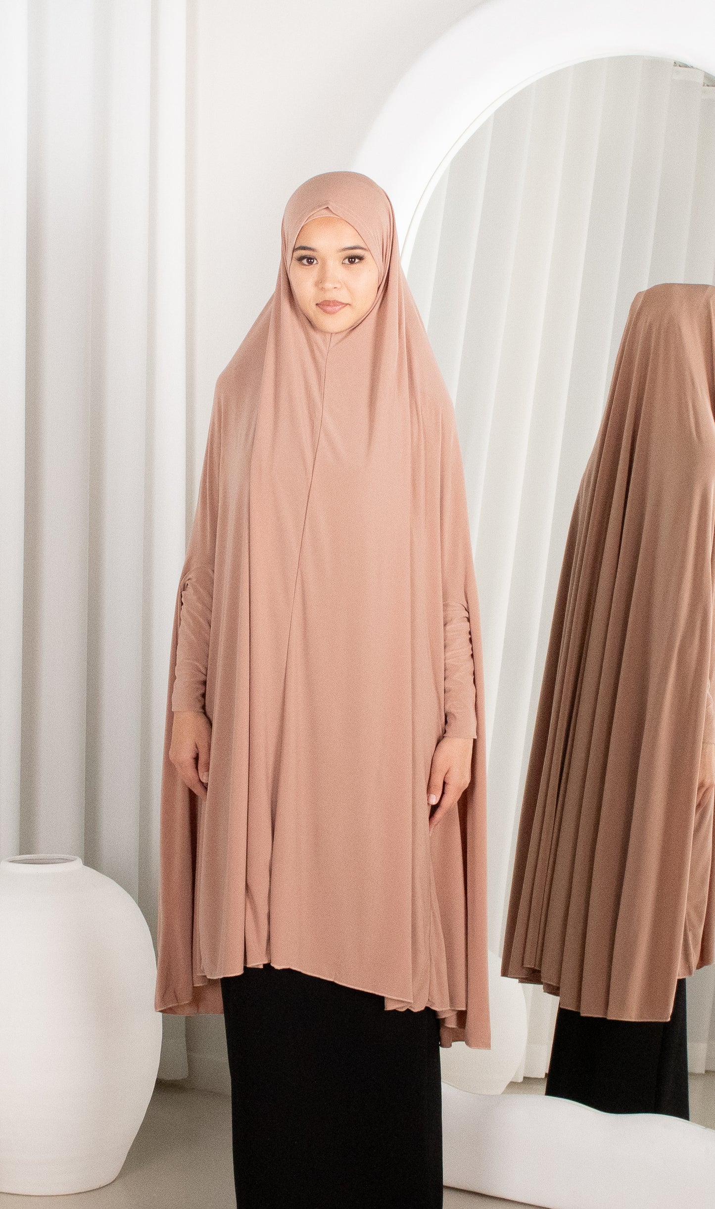 Woman wearing a beige hijab with a white curtain background