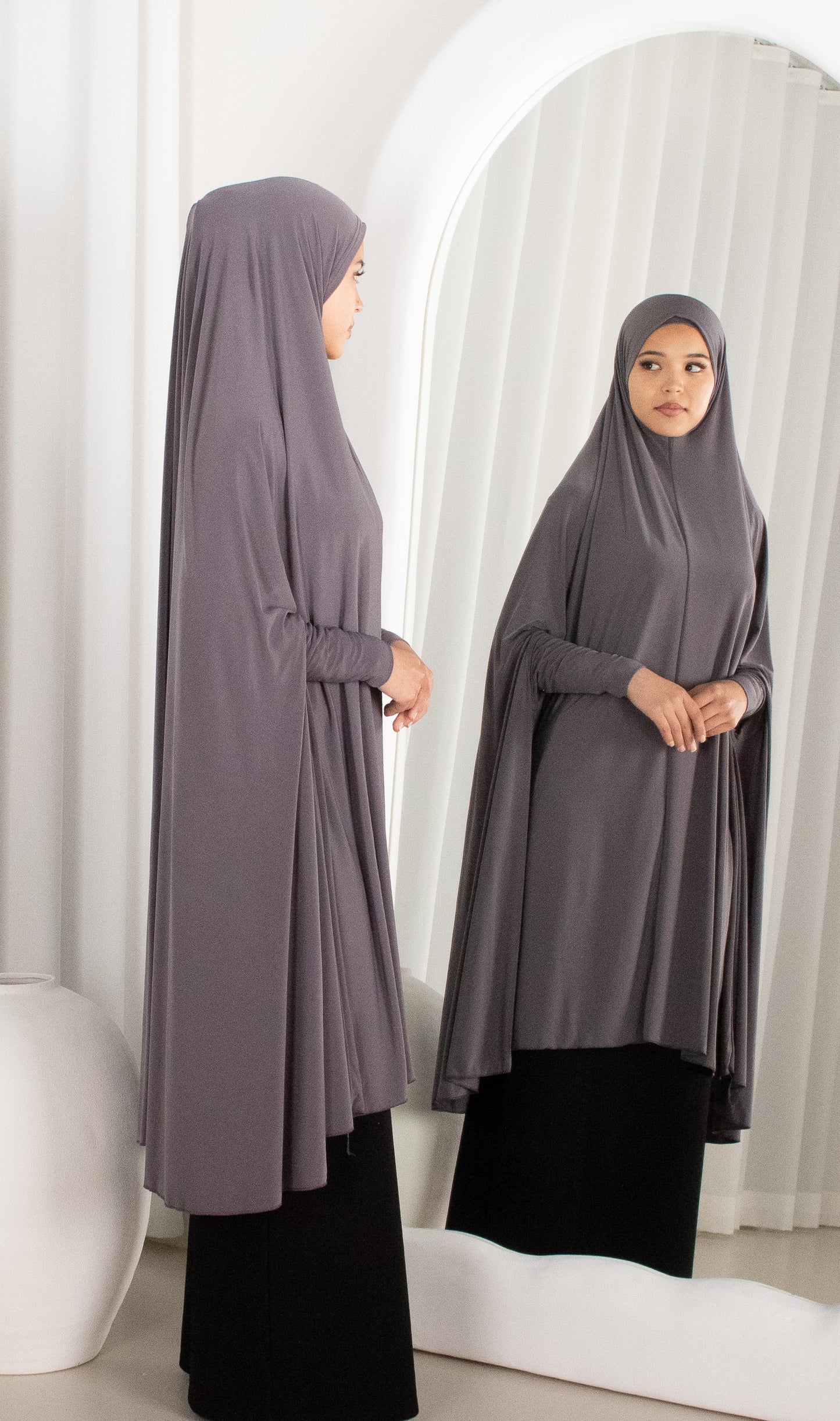 Woman wearing a gray abaya standing in front of a mirror.