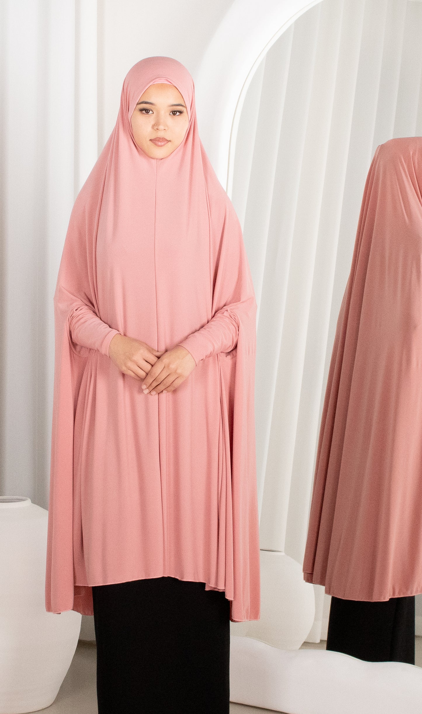Woman wearing a pink hijab and dress against a white background