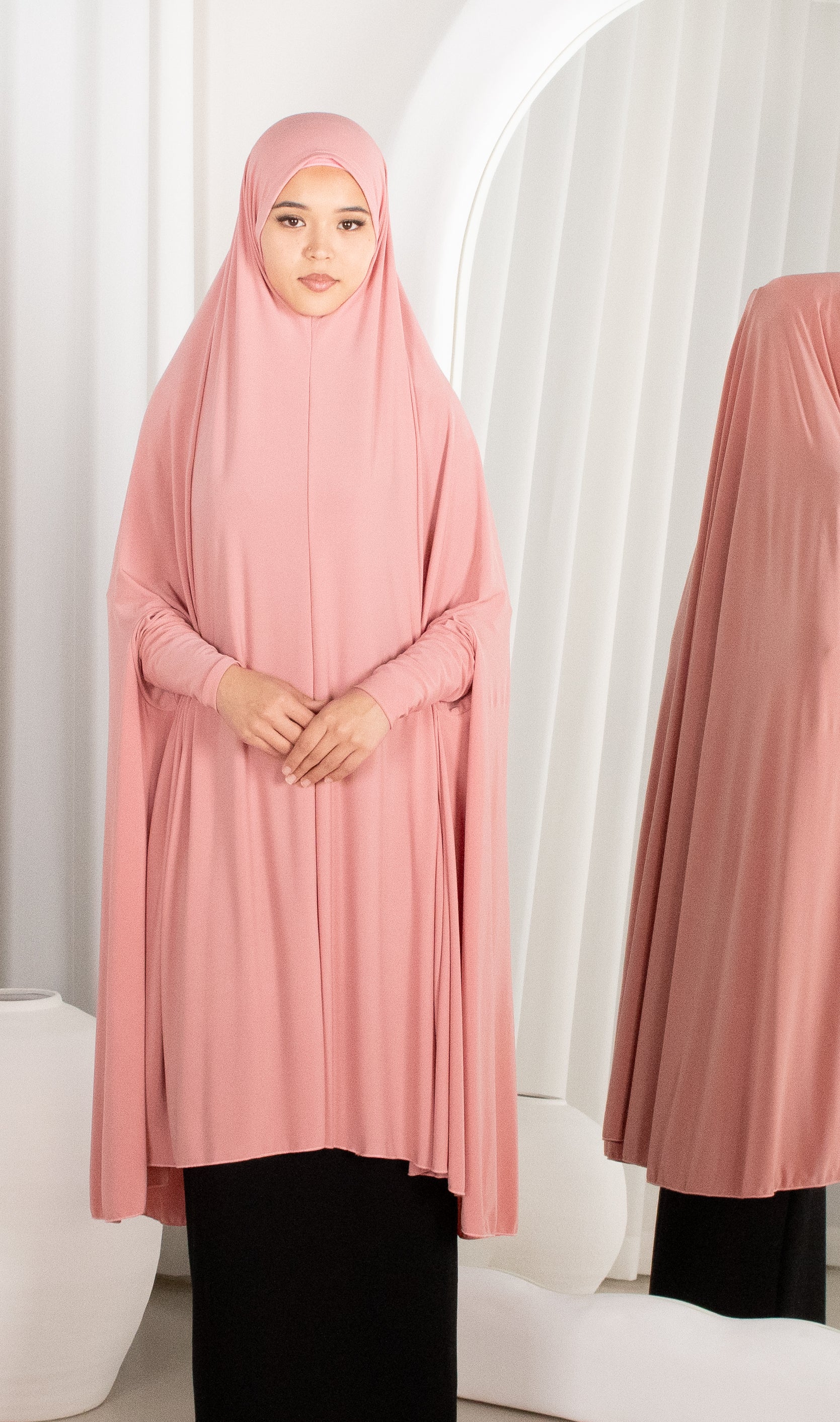 Woman wearing a pink hijab and dress against a white background