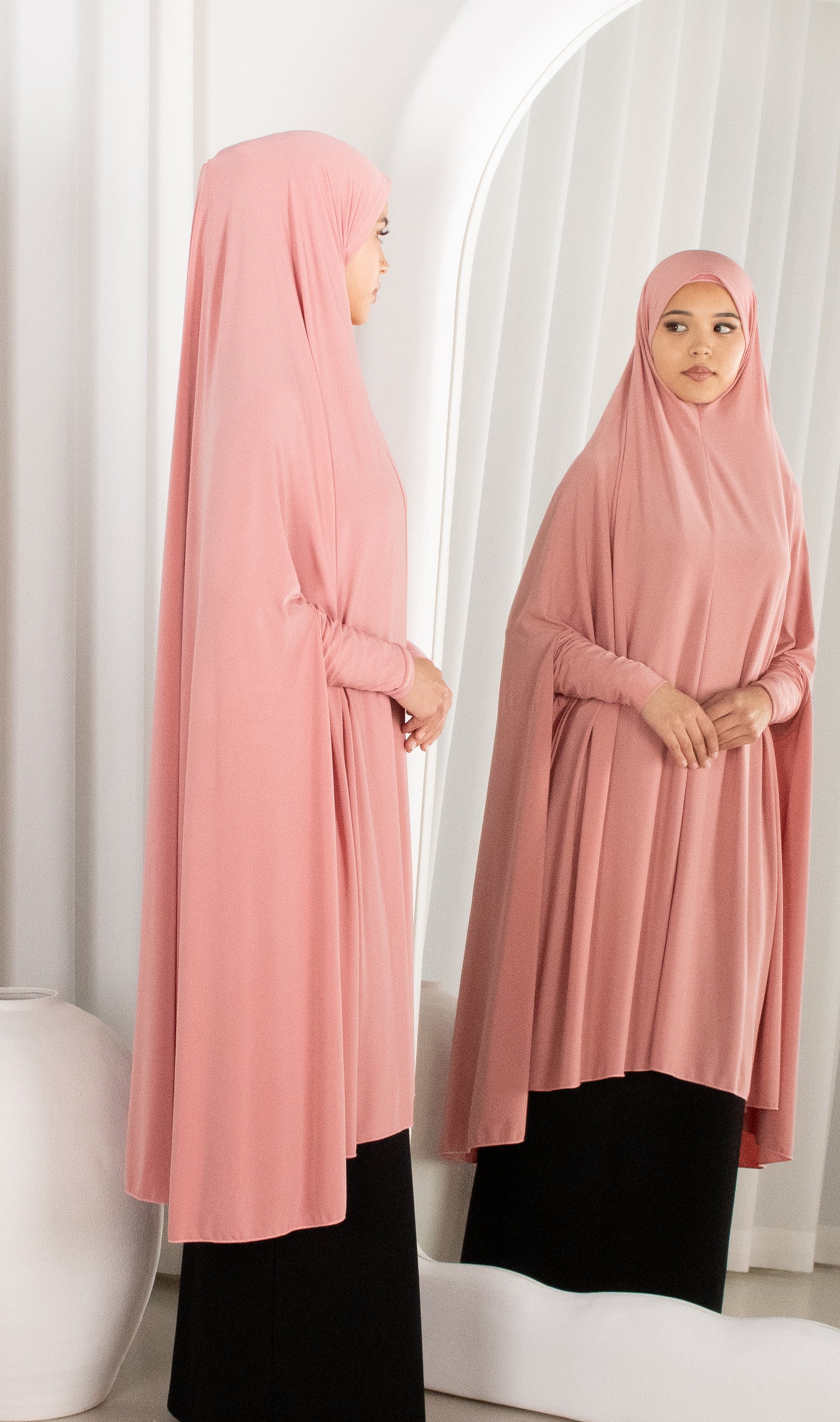 Woman wearing a pink hijab and black outfit standing in front of a mirror.