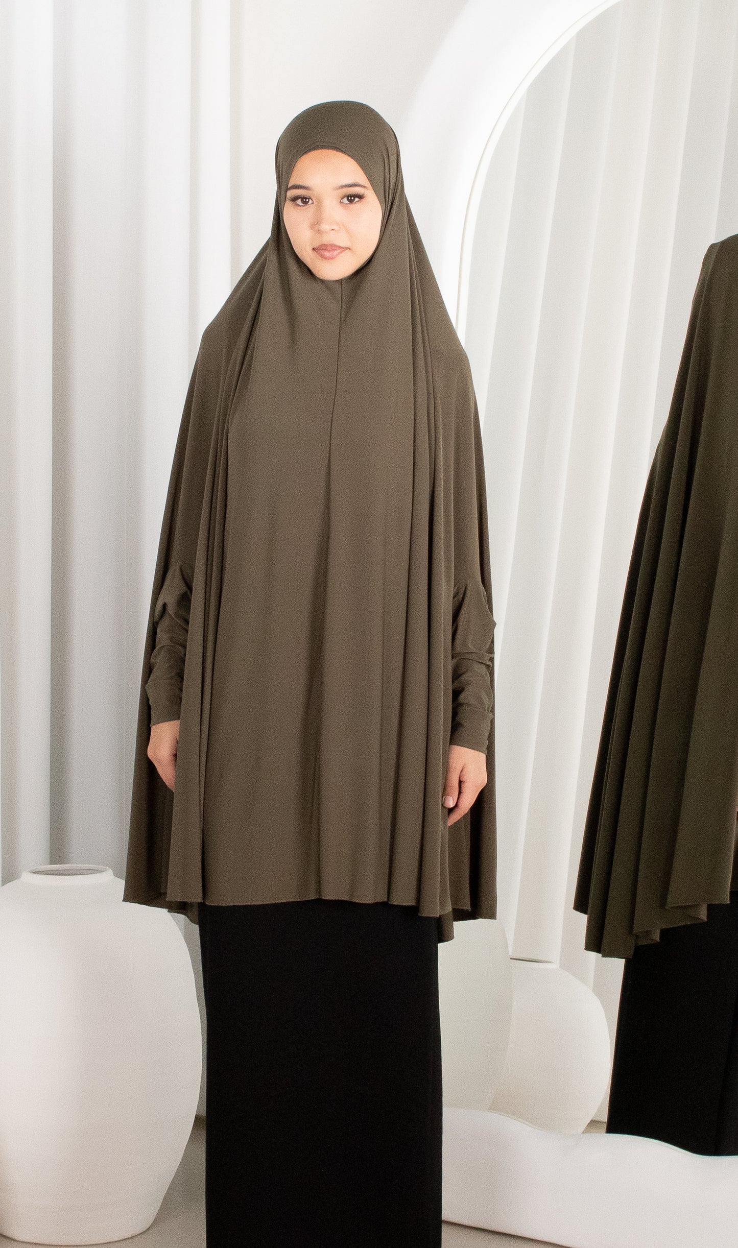 Woman wearing a brown hijab and dress in a white room