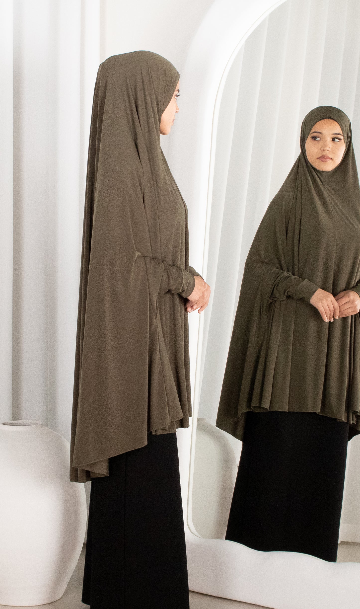 Woman wearing a brown hijab and black outfit standing in front of a mirror.