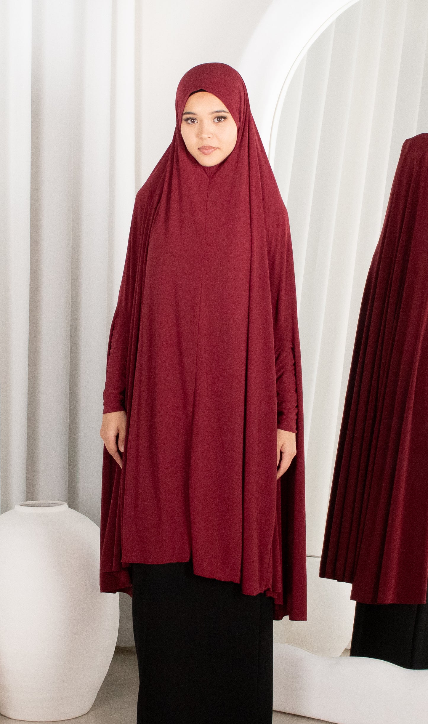 Woman wearing a burgundy hijab and dress in a minimalistic setting