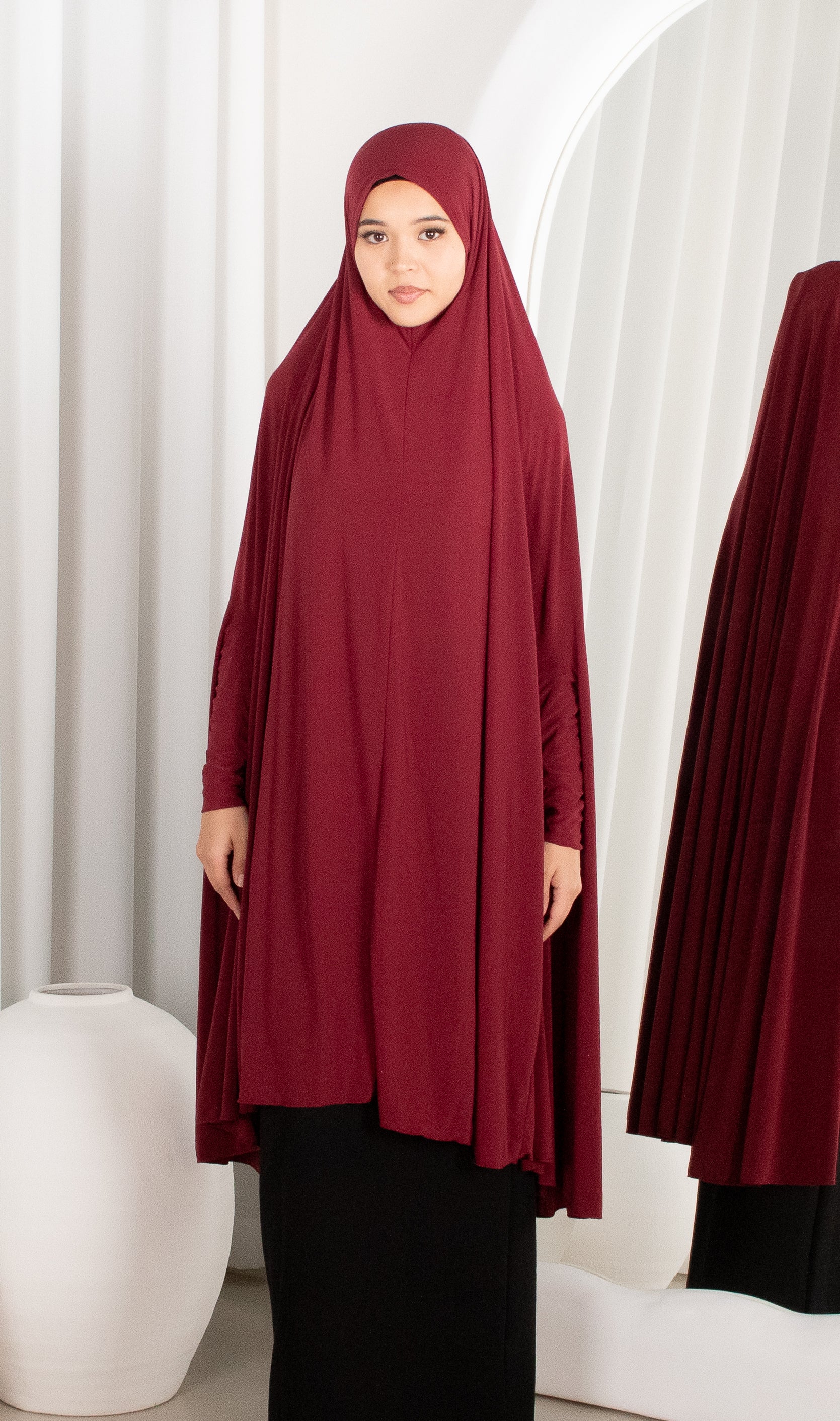 Woman wearing a burgundy hijab and dress in a minimalistic setting