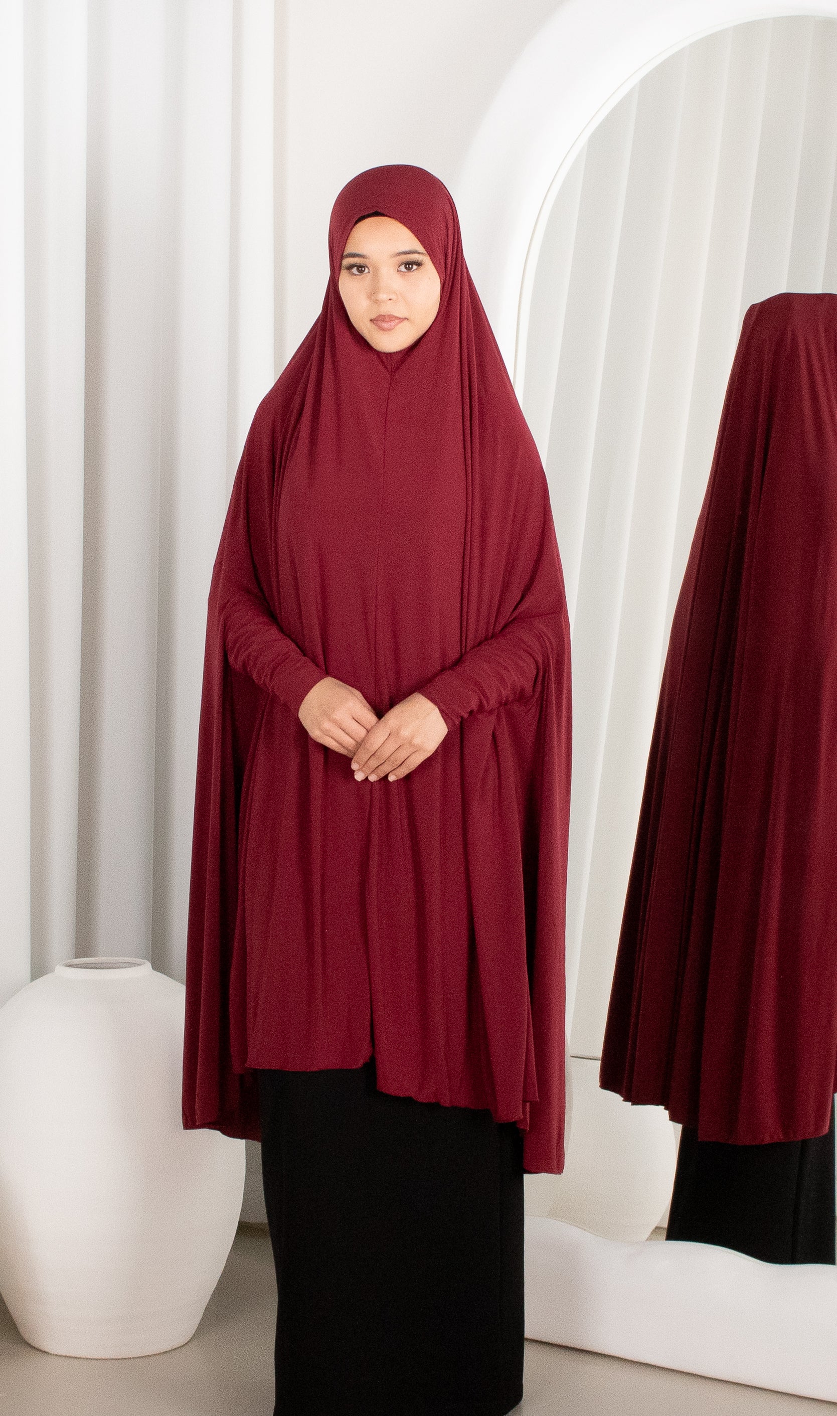 Person wearing a burgundy abaya in front of a white curtain