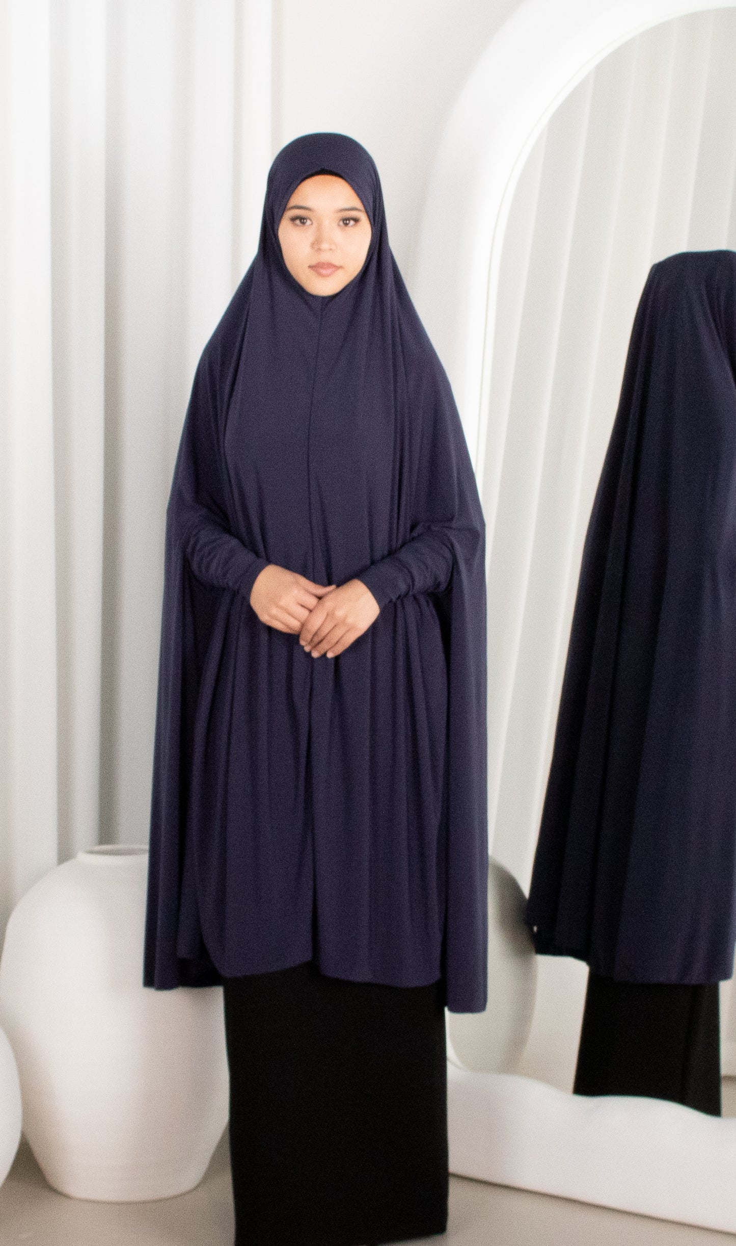 Woman wearing a navy abaya in front of a white curtain