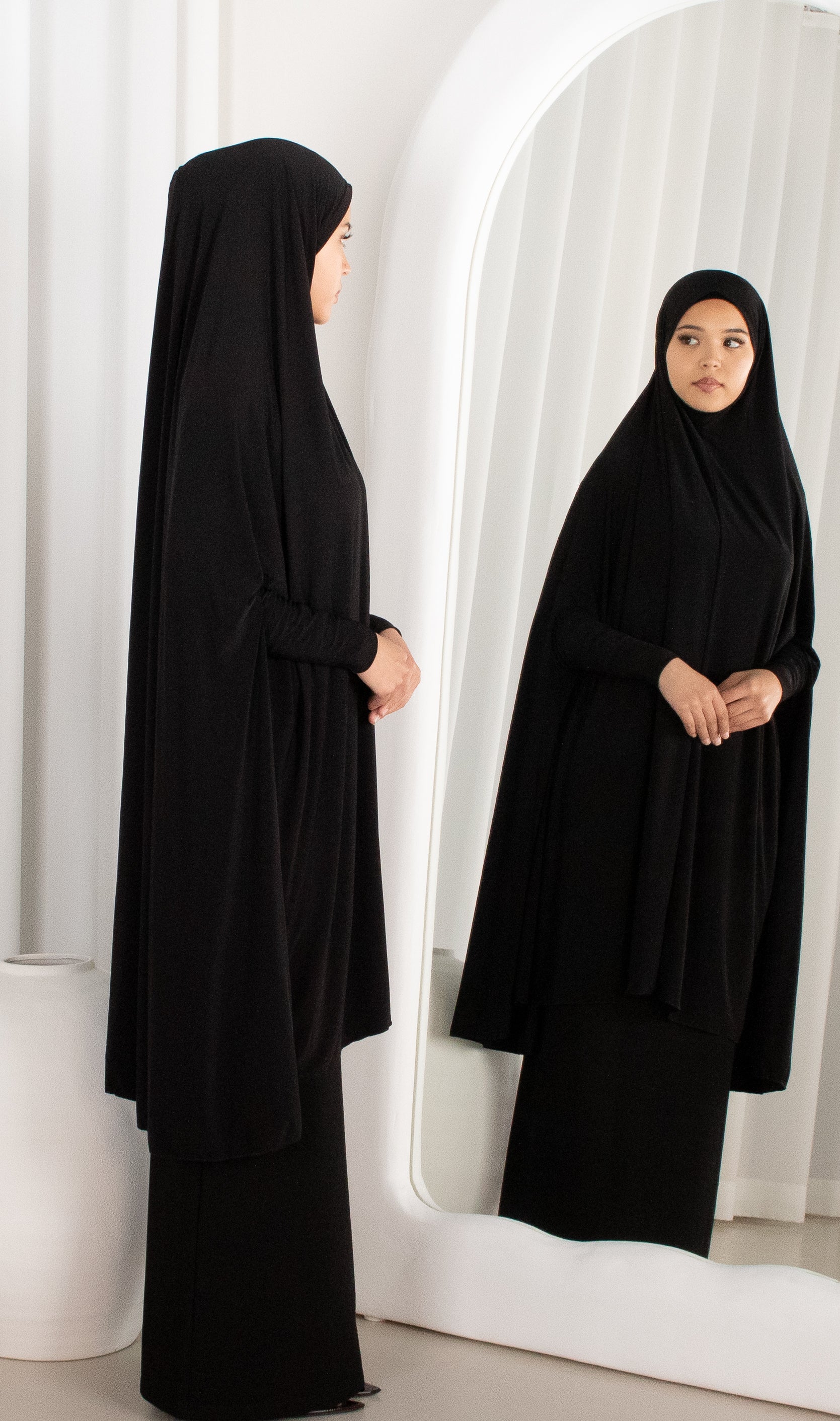 Woman wearing a black abaya standing in front of a mirror.