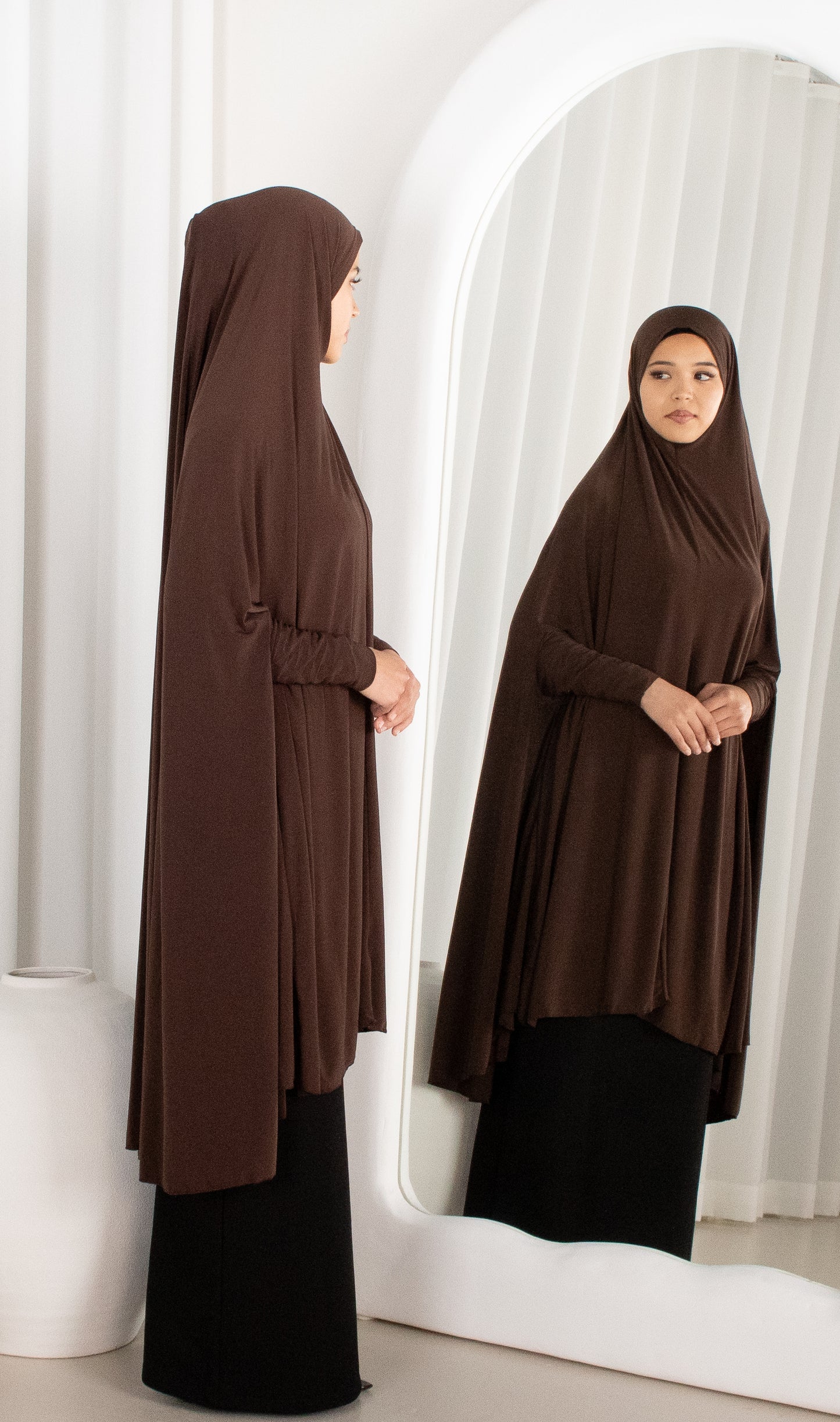 Woman wearing a brown abaya standing in front of a mirror.
