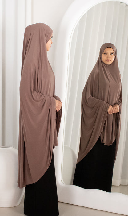 Woman wearing a brown hijab and black outfit standing in front of a mirror.
