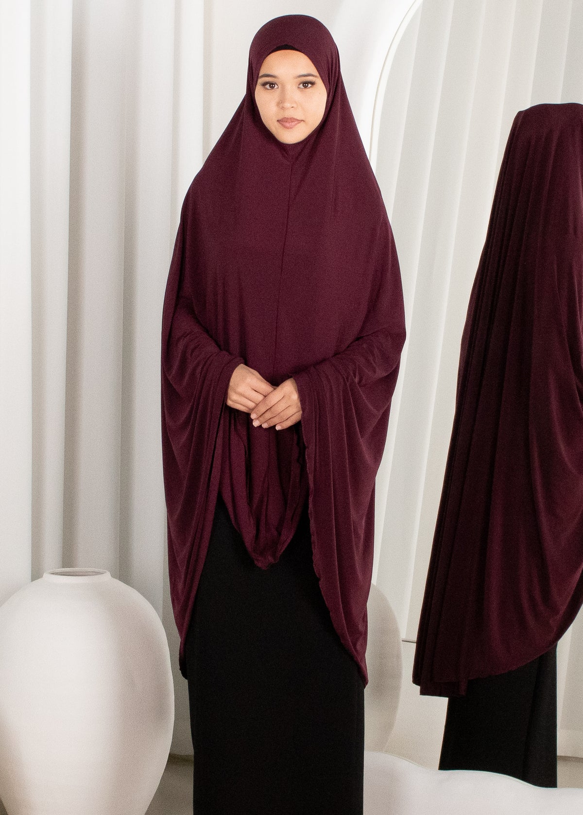 Woman wearing a burgundy hijab in front of white curtains