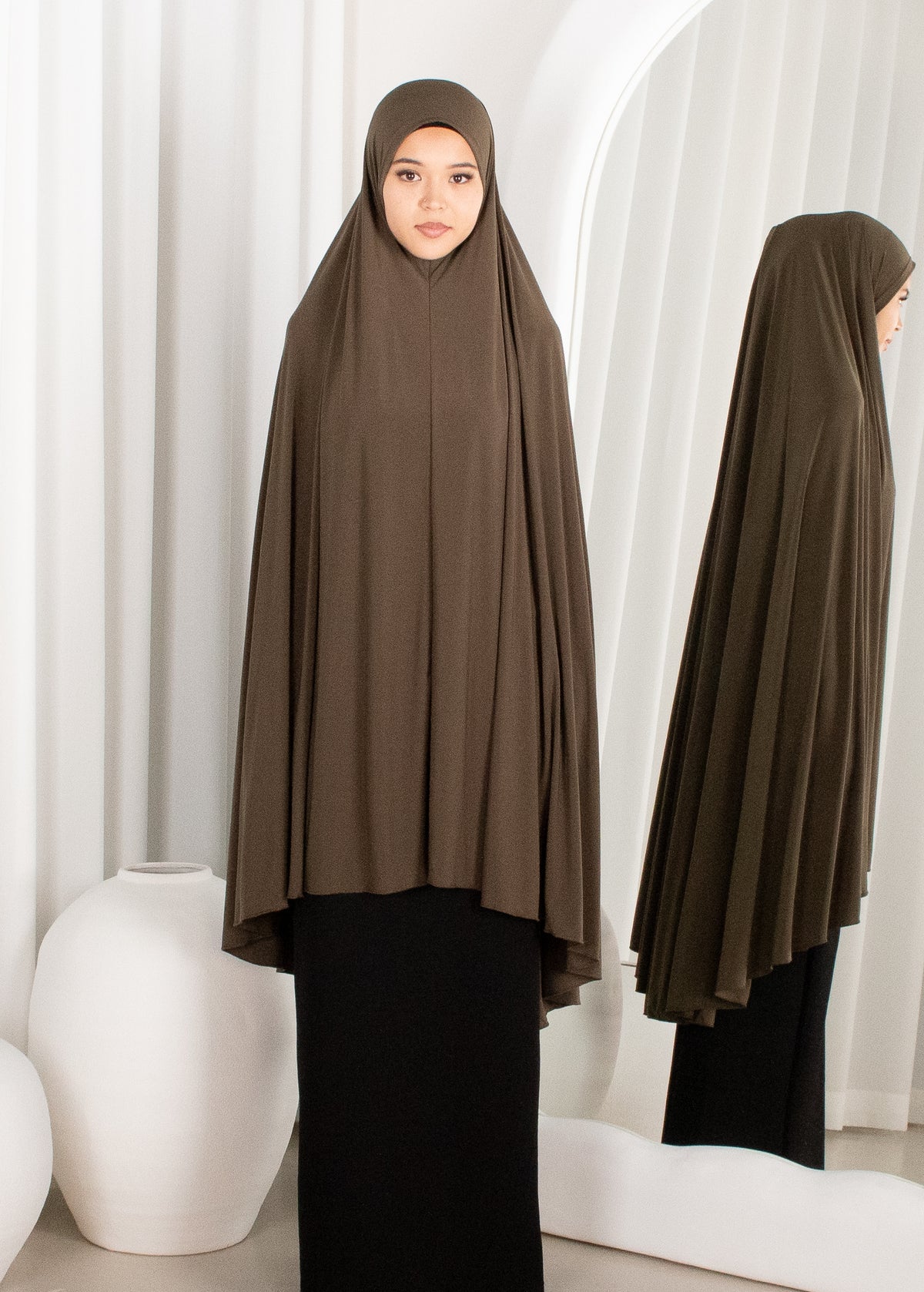 Woman wearing a brown hijab in front of white curtains