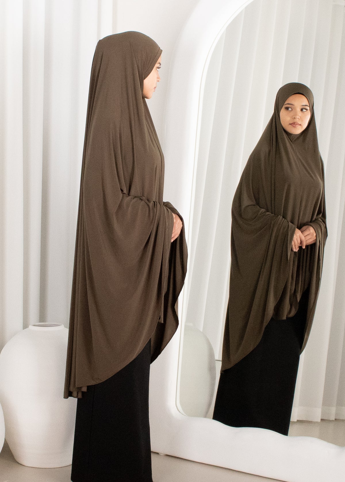 Woman wearing a brown hijab standing in front of a mirror.