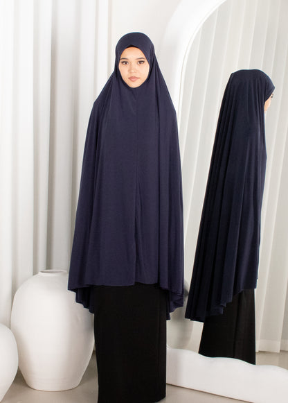 Woman wearing a navy blue hijab and black outfit in a minimalistic setting.