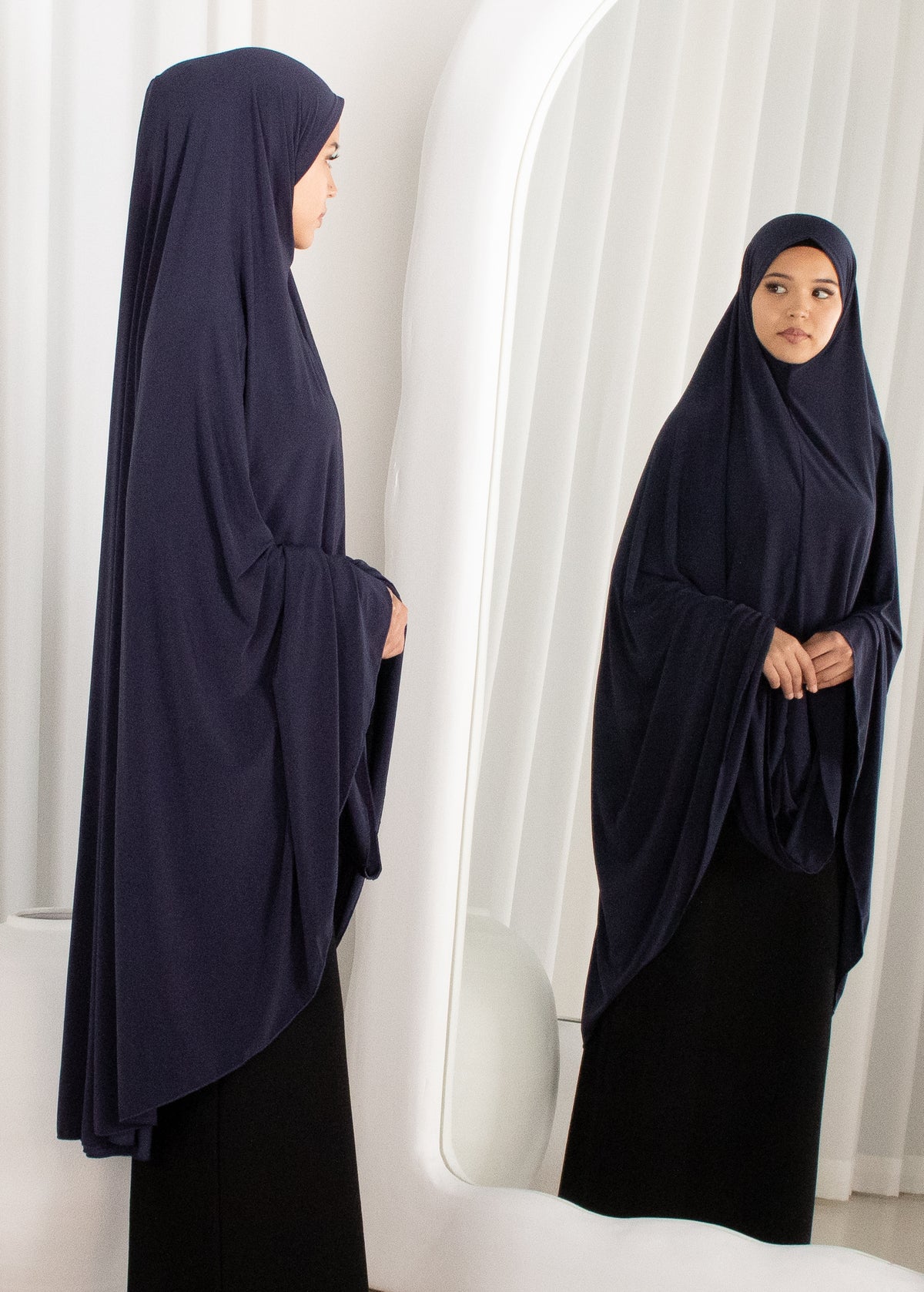 Woman wearing a navy blue hijab and black dress standing in front of a mirror.