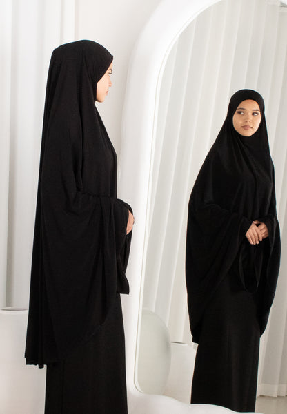 Woman wearing a black abaya in front of a white curtain
