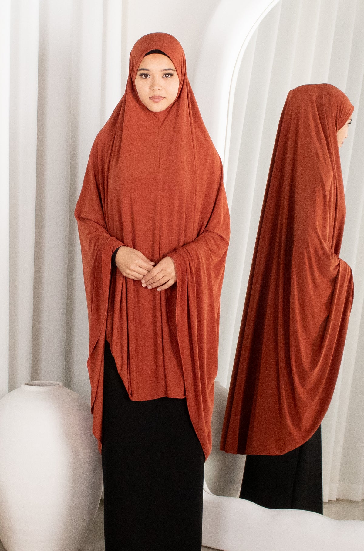 Woman wearing a rust-colored hijab in front of white curtains
