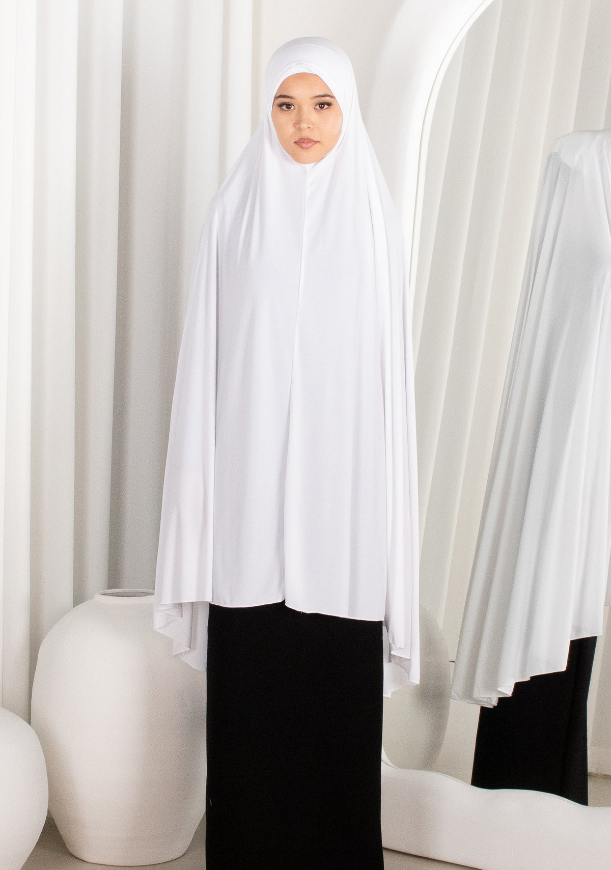 Woman wearing a white hijab and black outfit in a minimalistic setting