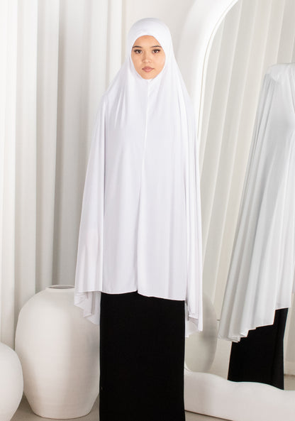 Woman wearing a white hijab and black outfit in a minimalistic setting