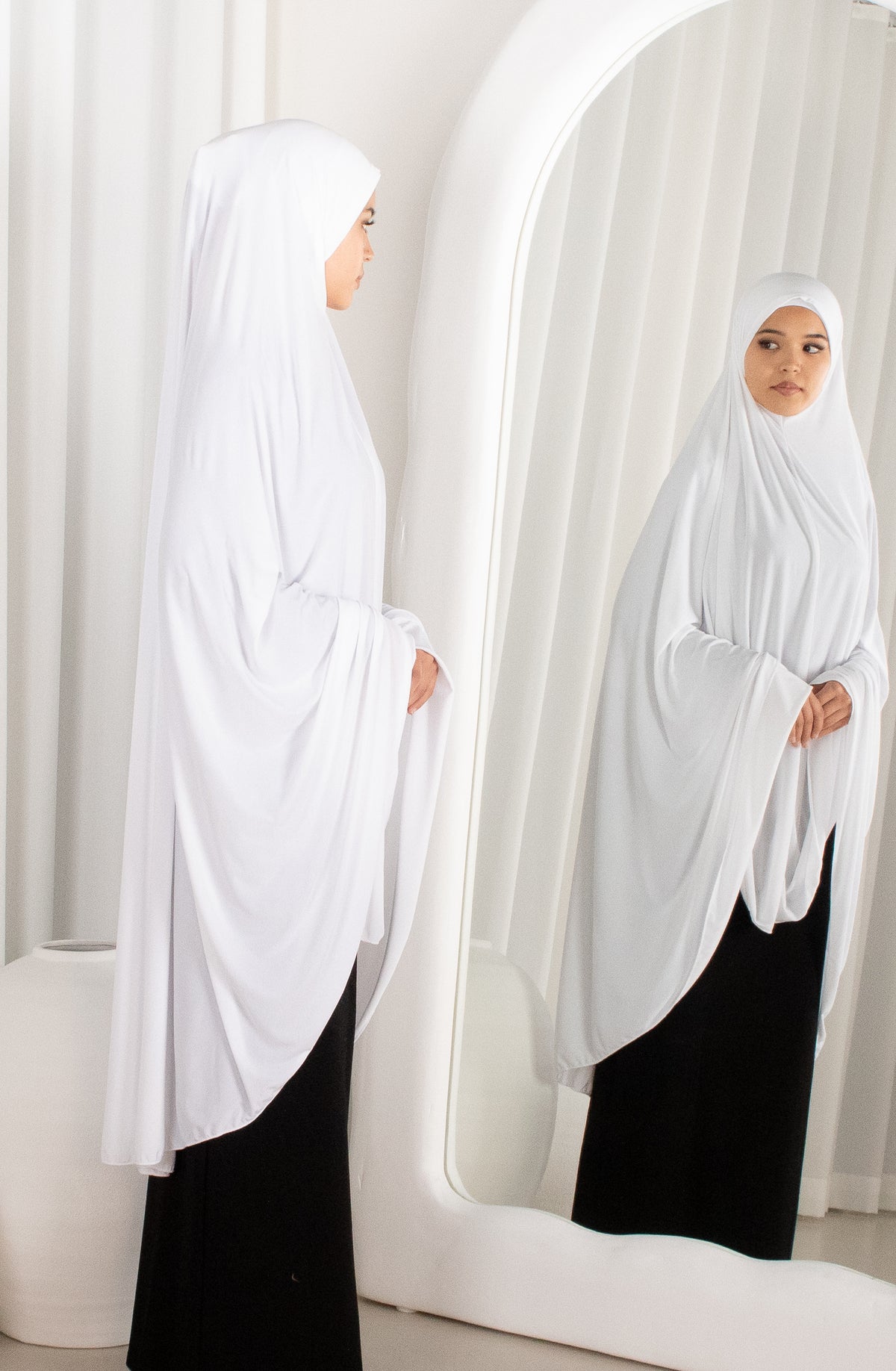 Woman wearing a white hijab in front of a mirror.