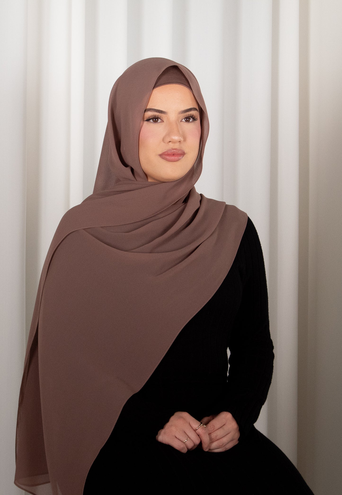 Woman wearing a brown hijab against a white curtain background