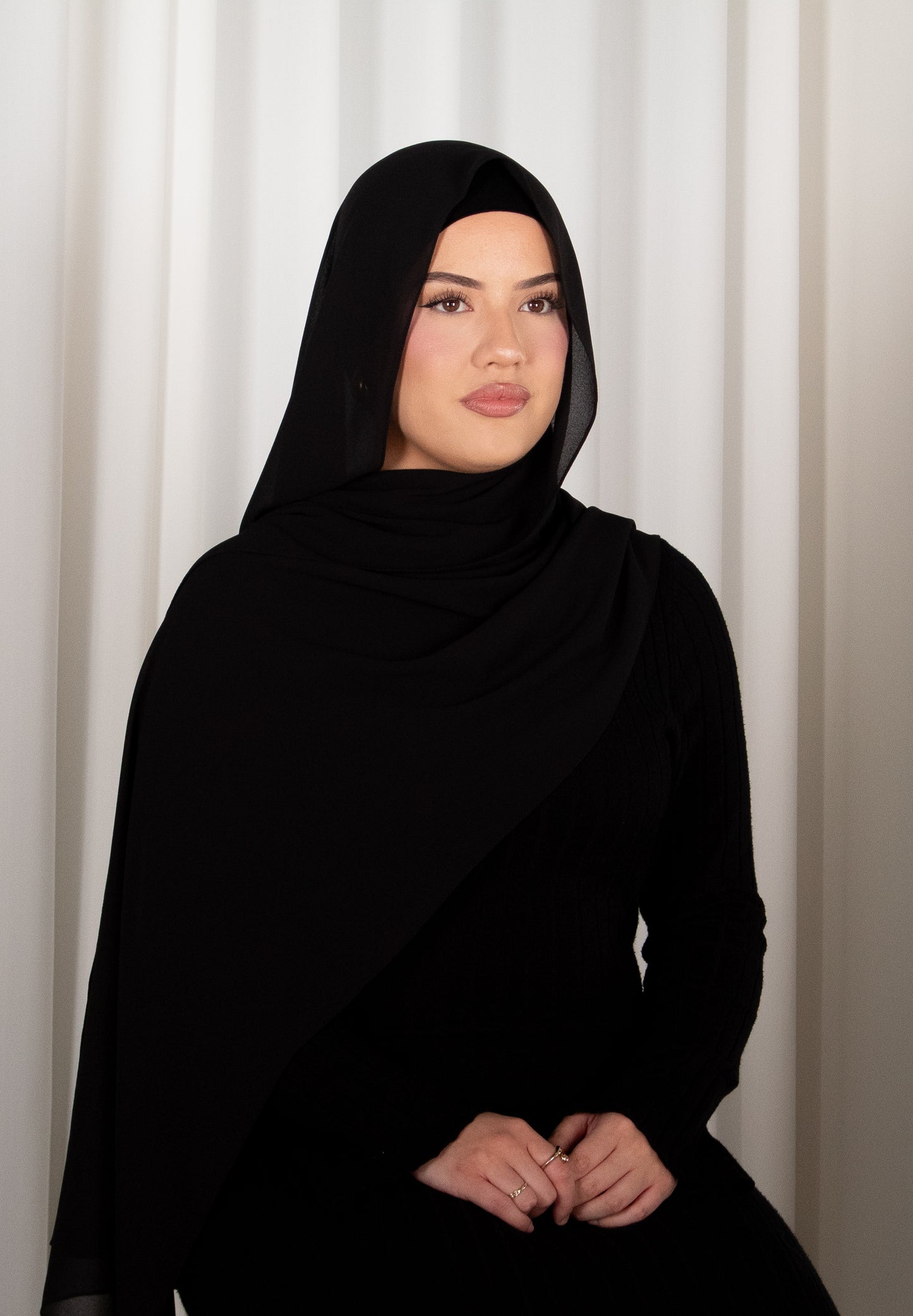 Person wearing a black hijab against a white curtain background