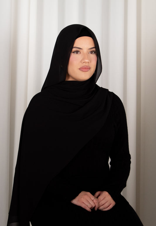 Person wearing a black hijab against a white curtain background