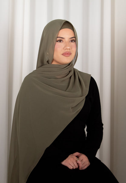 Woman wearing a green hijab and black outfit against a white curtain background