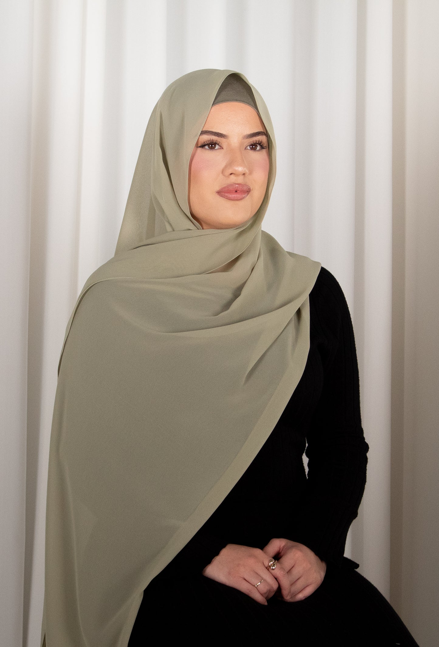 Woman wearing a light green hijab against a white curtain background